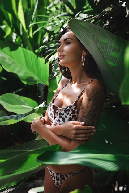 Piękne kobiece ciało o gładkiej skórze i zwartych biodrach w pobliżu zielonych liści palmowych.