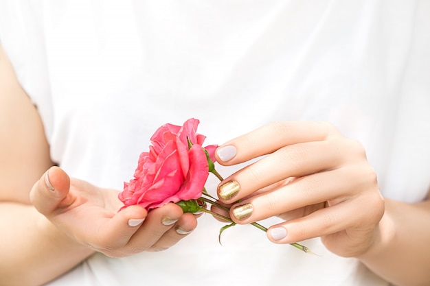 Piękne kobiece dłonie z doskonałym złotym i różowym wzorem na paznokcie trzymają świeży kwiat róży