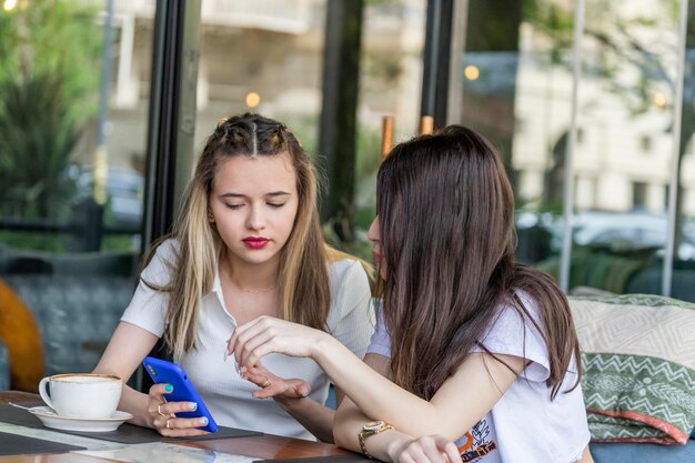 Piękne młode dziewczyny siedzą w restauracji i patrzą na swój telefon