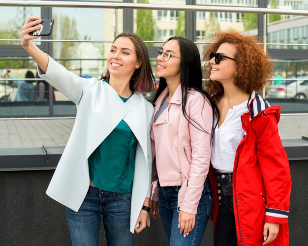 Piękne stylowe koleżanki biorąc selfie w smartfonie