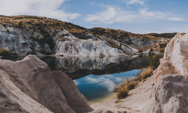 Bezpłatne zdjęcie piękne ujęcie blue lake w nowej zelandii otoczone skalistymi wzgórzami pod błękitnym niebem