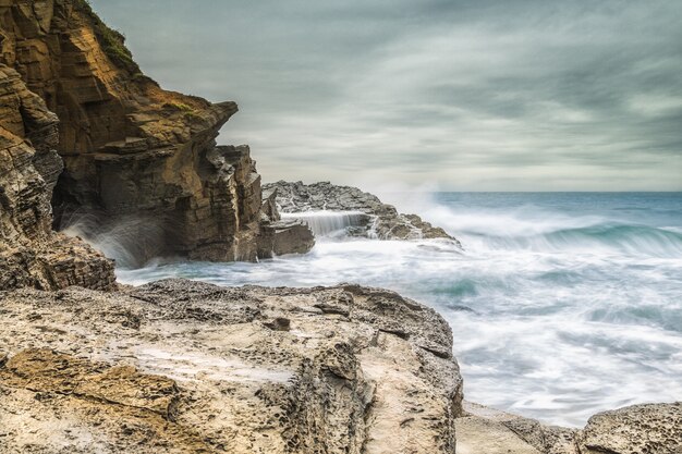 Piękne ujęcie fal morskich uderzających o skały na brzegu morza przy zachmurzonym szarym niebie