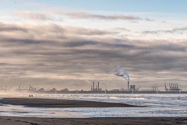 Bezpłatne zdjęcie piękne ujęcie morza z wiatrakami i fabryką w oddali pod pochmurnym niebem