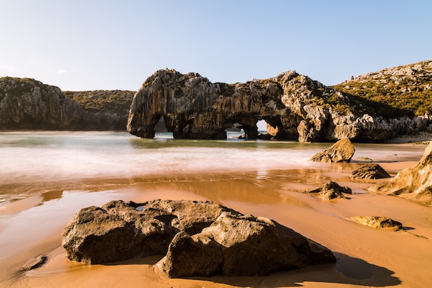 Piękne ujęcie naturalnych łuków skalnych w pobliżu piaszczystej plaży w słoneczny dzień