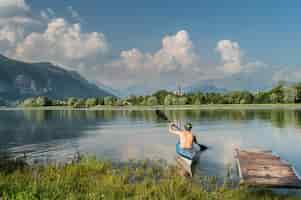 Bezpłatne zdjęcie piękne ujęcie osoby wiosłującej łodzią po jeziorze otoczonym drzewami i górami