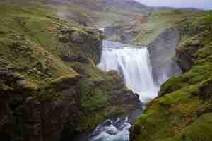 Bezpłatne zdjęcie piękne ujęcie wodospadu spływającego kaskadą po zielonych górach na islandii