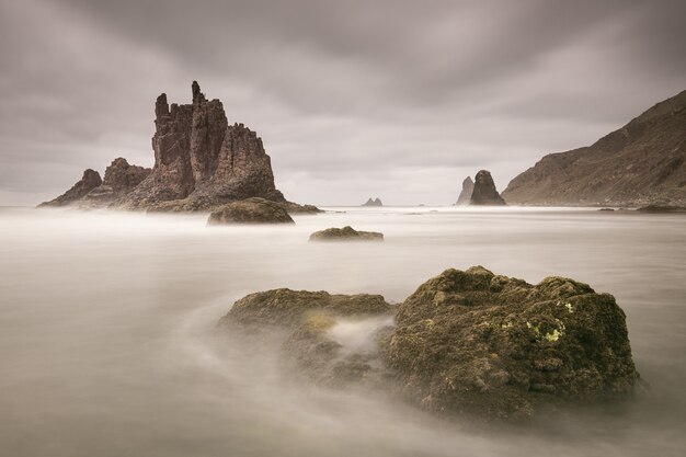 Piękne ujęcie wody opływającej duże kamienie w pobliżu skały Benijo w pochmurny dzień w Hiszpanii
