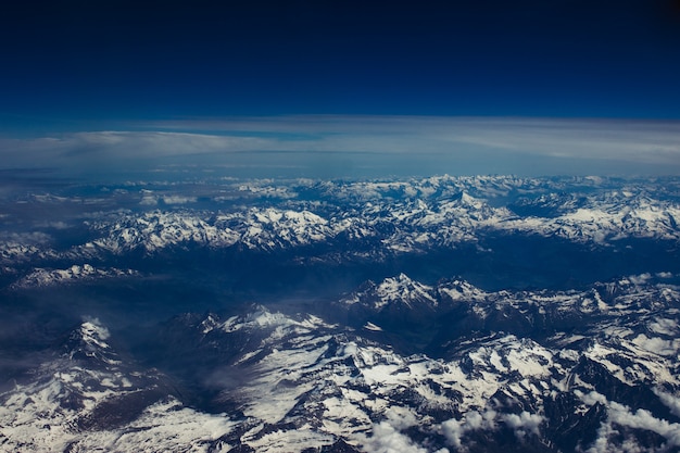 Piękne zdjęcie lotnicze śnieżnej, górskiej scenerii pod zapierającym dech w piersiach błękitnym niebem
