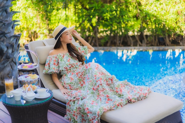 Pięknego portreta młoda azjatykcia kobieta z popołudniowym herbacianym ustawiającym z kawą siedzi na krześle wokoło pływackiego basenu
