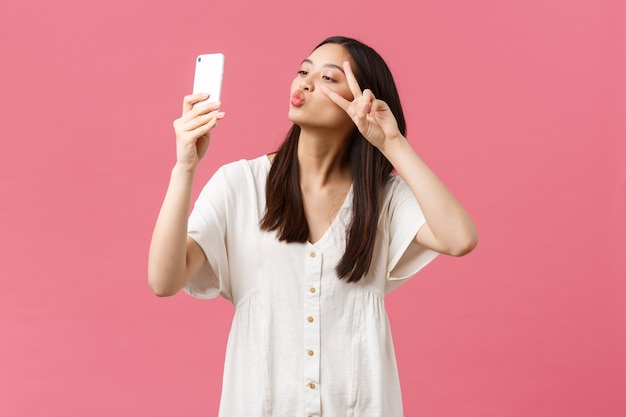 Piękno, Ludzie Emocje I Koncepcja Technologii. Kobieca, Atrakcyjna Stylowa Azjatycki Dziewczyna Blogger Biorąc Selfie Na Aparacie Smartfona, Uśmiechając Się Zadowolony Na Telefon Komórkowy, Stojąc Na Różowym Tle.