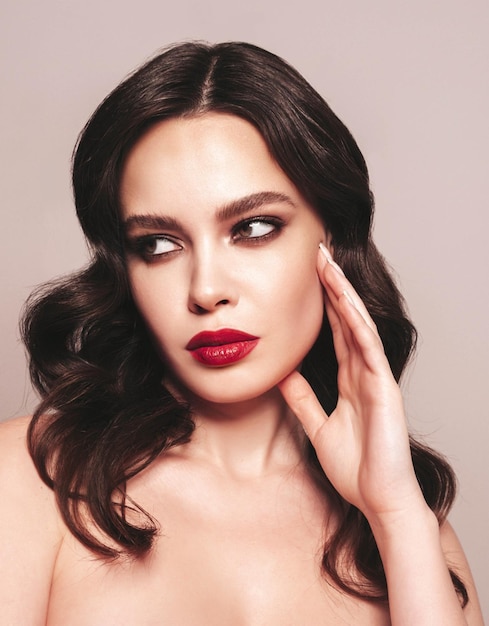Piękno portret młodej kobiety brunetka z wieczorowym makijażem i idealną czystą skórą seksowny model z kręconymi włosami pozowanie w studio z czerwonymi jasnymi naturalnymi ustami na białym tle
