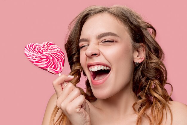 Piękno portret słodkiej dziewczyny w akcie do jedzenia cukierka na różowej ścianie