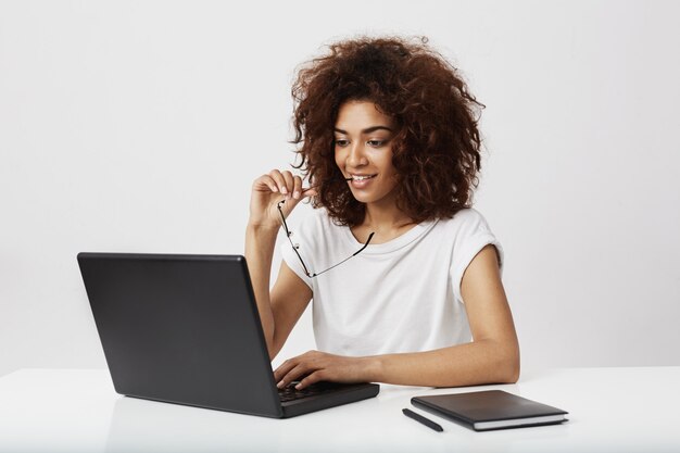 Piękny afrykański bizneswoman patrzeje laptopu ekran nad biel ścianą.