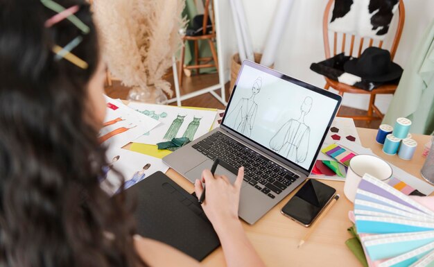 Piękny azjatycki projektant mody rysujący szkice do nowej kolekcji na laptopie komputerowym