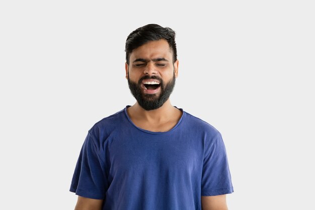Piękny męski portret w połowie długości na białym tle na białej ścianie. Młody emocjonalny człowiek hinduski w niebieskiej koszuli. Wyraz twarzy, ludzkie emocje, koncepcja reklamy. Krzyczenie lub śmiech.