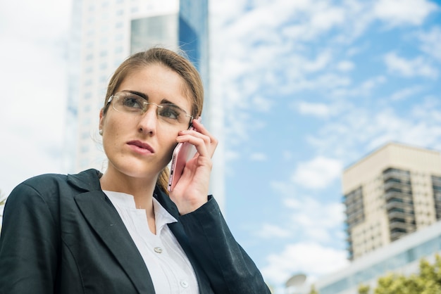 Piękny młody bizneswoman opowiada na telefon komórkowy pozyci przeciw niebu