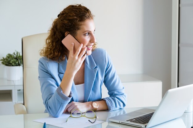 Piękny młody bizneswoman używa jej telefon komórkowego w biurze.