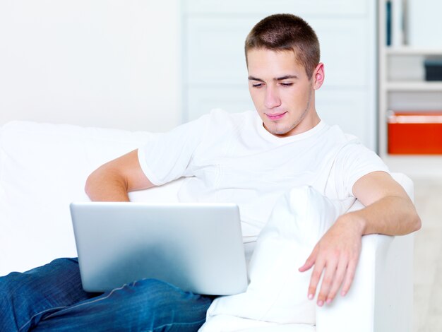 Piękny, młody chłopak patrzy w laptopie w domu