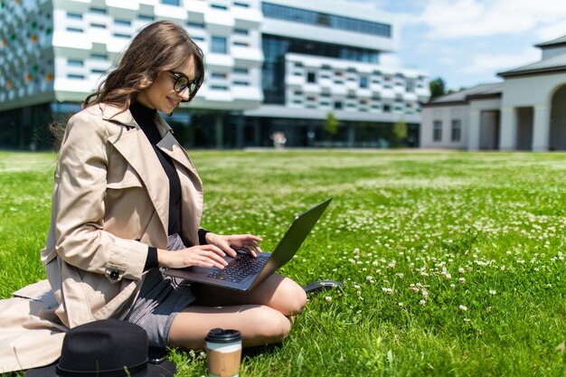 Piękny młody student za pomocą laptopa na trawie w kampusie