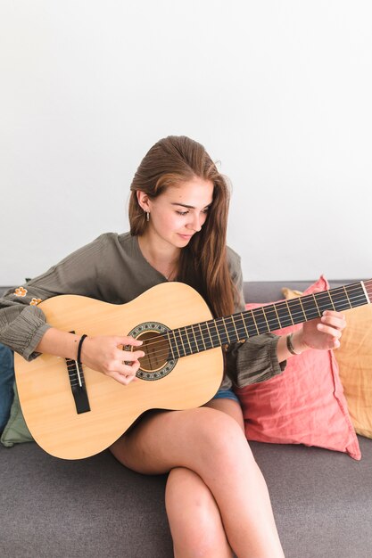 Piękny nastoletniej dziewczyny obsiadanie na kanapie bawić się gitarę
