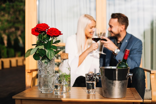 Piękny para siedzi za wazonem czerwona róża i butelka wina w wiaderku lodu