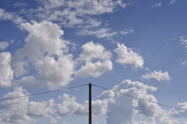 Bezpłatne zdjęcie piękny strzał białe chmury na niebieskim niebie z słupem prądu w środku