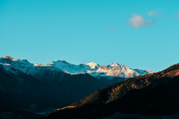 Piękny strzał zalesieni wzgórza i śnieżna góra w odległości z niebieskim niebem