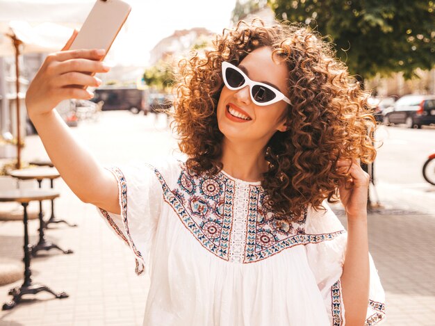 Piękny uśmiechnięty model z fryzurą afro loki, ubrany w letnią białą sukienkę hipster.