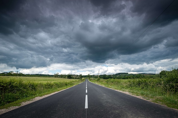 Piękny widok na pustą drogę otoczoną zielenią pod ciemnymi burzowymi chmurami