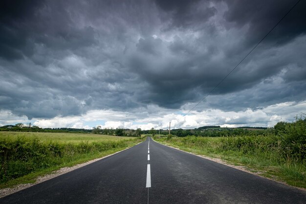 Piękny widok na pustą drogę otoczoną zielenią pod ciemnymi burzowymi chmurami