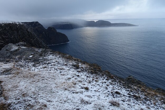 Piękny widok na zamglone, pokryte śniegiem klify na wybrzeżu Norwegii