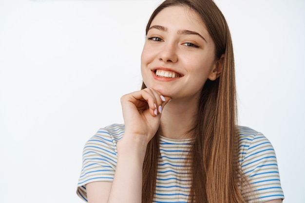 Bezpłatne zdjęcie pielęgnacja i uroda skóry. szczęśliwa uśmiechnięta dziewczyna z białymi zębami i czystą naturalną skórą, patrząc na kamery, stojąc w koszulce w studio.