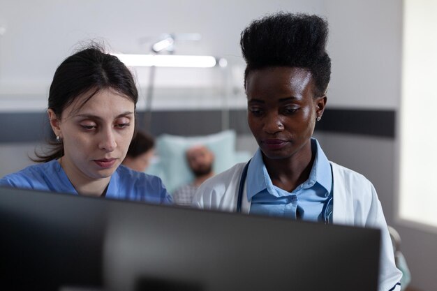 Pielęgniarka i lekarz afroamerykański przy użyciu komputera osobistego do obrazowania klinicznego w prywatnym oddziale szpitalnym dla pacjentów. Lekarz konsultujący się z pacjentem podczas gdy dyżurny i opiekun odczytuje cyfrowe wyniki laboratoryjne.