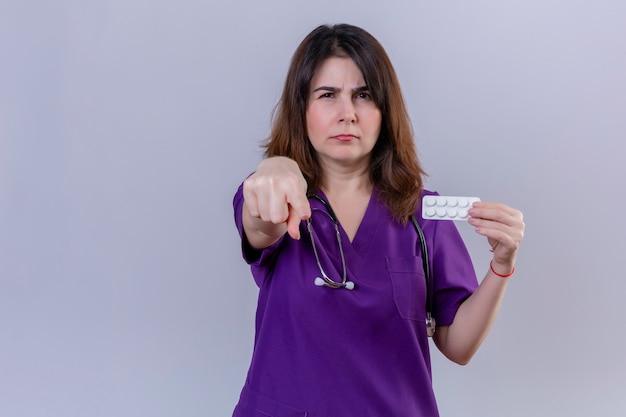Bezpłatne zdjęcie pielęgniarka kobieta w średnim wieku na sobie mundur medyczny i stetoskop gospodarstwa blister z pigułkami wskazującymi niezadowolony
