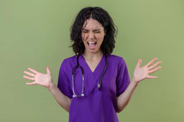 pielęgniarka ubrana w mundur i stetoskop szalony i szalony krzyczący i wrzeszczący z agresywnym wyrazem twarzy i rękami wzniesionymi na odizolowanej zieleni
