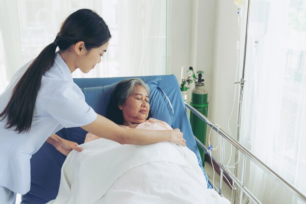 Pielęgniarki dobrze opiekują się starszymi pacjentkami w łóżku szpitalnym, odczuwają szczęście - koncepcja medyczna i opieki zdrowotnej