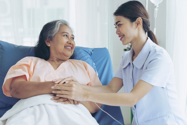 Pielęgniarki dobrze opiekują się starszymi pacjentkami w łóżku szpitalnym, odczuwają szczęście - koncepcja medyczna i opieki zdrowotnej