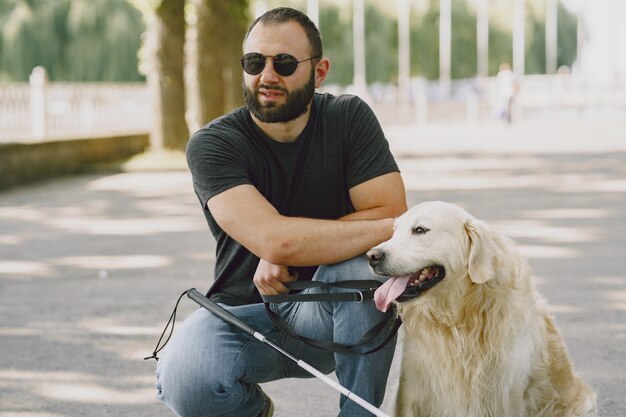 Pies przewodnik pomagający niewidomemu w mieście. Przystojny ślepy facet odpoczywa z golden retriever w mieście.