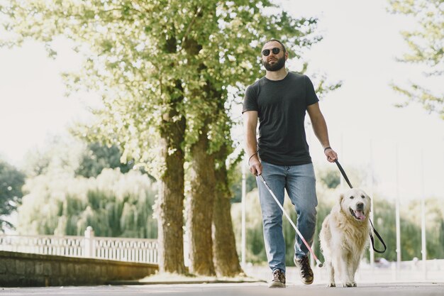 Pies przewodnik pomagający niewidomemu w mieście. Przystojny ślepy facet odpoczywa z golden retriever w mieście.