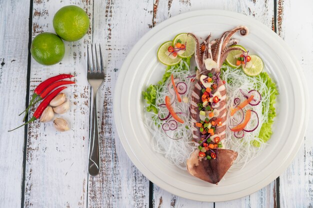 Bezpłatne zdjęcie pikantna kałamarnica cytrynowa z galangą, chilli, marchewką, miętą pieprzową, dymką i czosnkiem na talerzu na białej drewnianej podłodze.