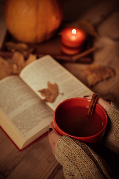 Pionowe ujęcie dłoni kobiety trzymającej filiżankę herbaty na stole z jesiennym liściem na książce