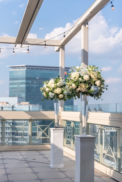 Pionowe ujęcie dwóch wazonów z pięknymi kwiatami na białych kolumnach na dachu budynku