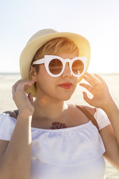 Pionowe ujęcie kobiety w białych okularach przeciwsłonecznych i kapeluszu zrobione na plaży