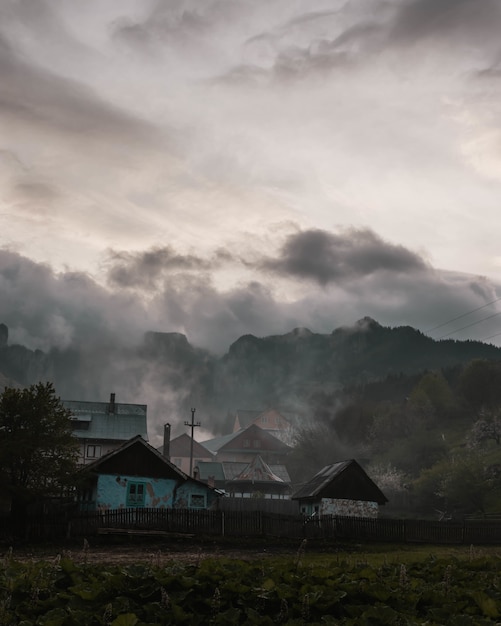 Pionowe ujęcie małej wioski z niesamowitymi górami skalistymi otoczonymi naturalną mgłą i chmurami