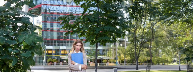 Bezpłatne zdjęcie pionowe ujęcie młodej bizneswoman w beżowym garniturze trzymającej dokumenty w rękach i wyglądającej pewnie