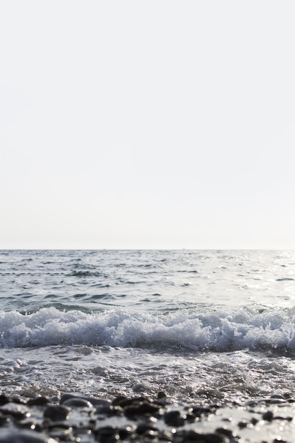 Bezpłatne zdjęcie pionowe ujęcie morza z pięknymi falami i czystym białym niebem