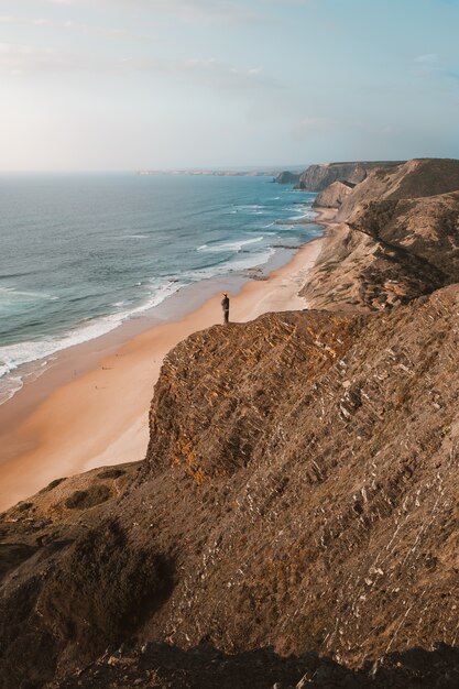 Pionowe ujęcie osoby na klifie patrząc na piękny ocean w Algarve, Portugalia