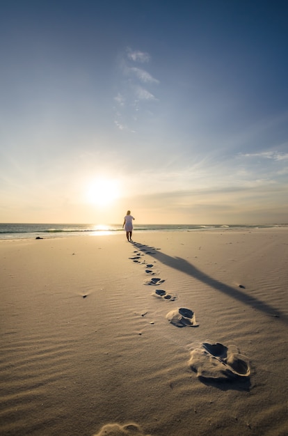Pionowe ujęcie osoby spacerującej po piaszczystej plaży ze śladami na pierwszym planie