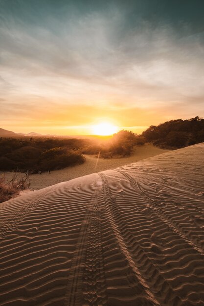 Pionowe ujęcie piaszczystych wzgórz na pustyni z zapierającym dech w piersiach zachodem słońca