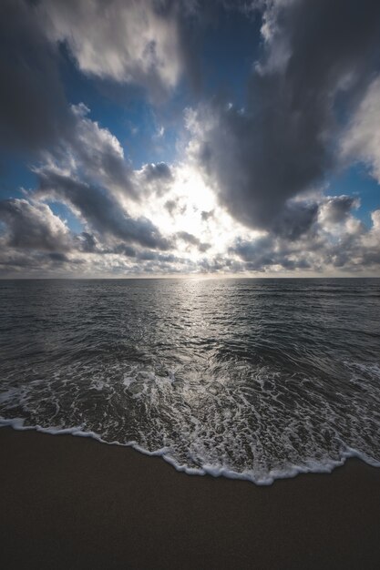 Pionowe ujęcie plaży otoczonej morzem pod błękitnym pochmurnym niebem